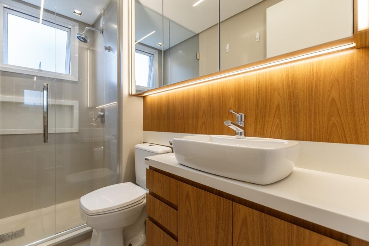 Banheiro da suíte com revestimentos originais em porcelanato fendi, bancada de silestone branco e móvel de marcenaria. Iluminação em LED e nicho embutido no box trazem funcionalidade e conforto ao design.